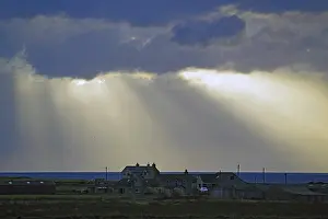 Scottish Coastal Landscape Drucke: Sunbeams break through dramatic clouds over houses by the sea