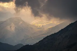 Weather Forecast Images Drucke: Sunlight pierces through dramatic storm clouds over a mountain landscape