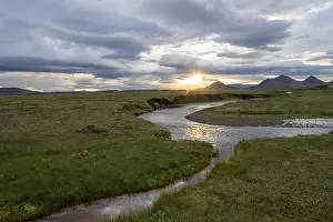 Sunset In Iceland Drucke: Sunset between clouds, river flowing through meadows