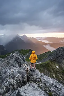 Mountain Peak Viewpoint Drucke: Sunset, hiker looking at mountains and peaks under dramatic clouds