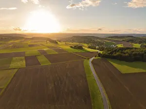 Dramatic Evening Sky Drucke: Sunset over sweeping fields with a winding road and dramatic sky