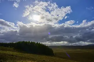 Scottish Highland Travel Photos Drucke: Sunshine and clouds over a forest on a clear sky