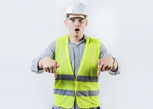 Young Engineer Drucke: Surprised engineer pointing down advertising space isolated