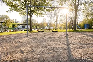 Atmospheric Evening Skies Drucke: Swing set on sandy ground in the evening light with trees in the background