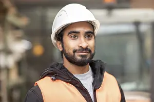 Young Technician In Workshop Drucke: Technician with beard and helmet works in a workshop