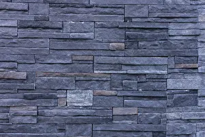 Urban Building Exterior View Drucke: A textured wall made of dark stone bricks arranged in a pattern