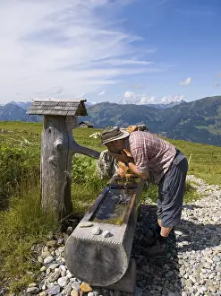 Mountainous Leisure Activity Drucke: Thirsty hiker drinking from a well