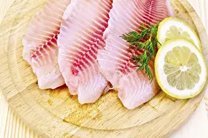 Drucke von Tilapia-Filets mit einem Zweig Dill, Zitrone gegen einen Holzbrett Tilapia Drucke: Tilapia-Filets mit einem Spritzer Dill.