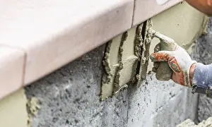 Pool Construction Site Drucke: Tile worker applying cement with trowel at pool construction site