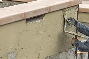 Real Estate Market Development Drucke: Tile worker applying cement with trowel at pool construction site
