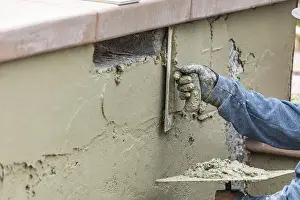 Swimming Pool Building Drucke: Tile worker applying cement with trowel at pool construction site