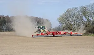 Springtime Agricultural Scene Drucke: Tractor with large ring roller surrounded by dust in a field in springtime in Ystad
