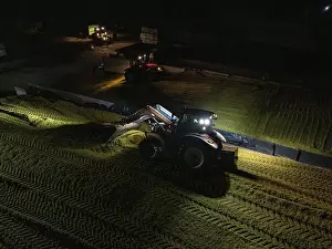 European Agricultural Machinery Drucke: A tractor with front loader illuminates the night on a field while working