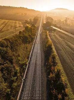 German Farmland Agriculture Drucke: Train tracks run through fields and trees in the light of the sunrise