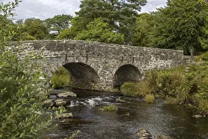Drucke von Zwei-bogiger Steinbrücke über einem Fluss, umgeben von Bäumen und Vegetation, in Dartmoor Nationalpark nahe Postbridge in Devon, Großbritannien Postbrücke Drucke: Zwei-bogiger Steinbrücke über einem Fluss.