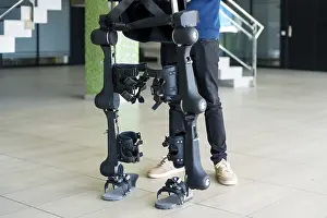 Modern Hospital Equipment Drucke: Unrecognizable computer engineer in mechanical exoskeleton looking at the robot with a tablet