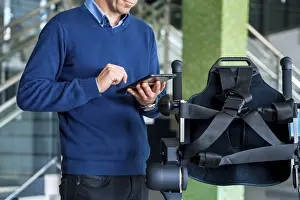 Physiotherapy Robot Drucke: Unrecognizable computer engineer in mechanical exoskeleton looking at the robot with a tablet