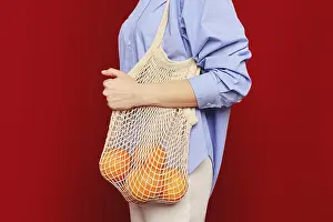 Sustainable Living Drucke: Unrecognizable woman holding oranges in a string bag on ruby red background