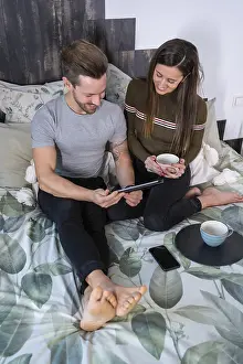 Couple Enjoying Coffee Together Drucke: Vertical top view of a couple drinking coffee and using tablet on the bed