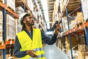 Supply Chain Management Drucke: Side view of an african worker scanning package with bar code reader in a distribution warehouse