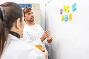 Young Scientists At Work Drucke: Side view of biologists using adhesives notes during a brainstorming in a laboratory