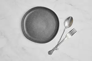 Still Life Studio Photography Drucke: Top view of empty ceramic plate and spoon with fork on marble background