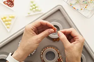 Handmade Jewelry Drucke: Top view of cropped unrecognizable woman's hands stringing beads on wire