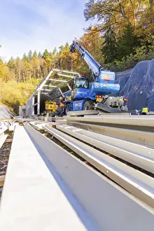 Hermann Hesse Railway Tunnel Drucke: View of large cranes working on a rail structure surrounded by trees