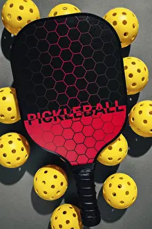 Modern Studio Shot Drucke: Top view of a paddle with a hexagonal pattern and bright yellow pickleballs on a dark background