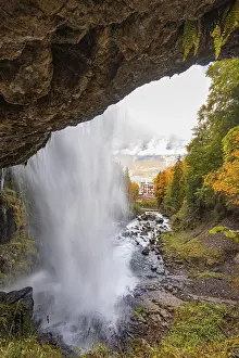 European Forest Landscapes Drucke: A waterfall flows through a forest with a view of a distant building