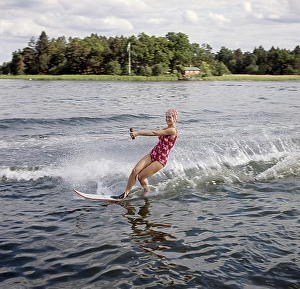Retro Swimwear Fashion Drucke: Waterskiing in the 1960s. A young woman in a patterned bathing suit passes the photographer on her waterskis