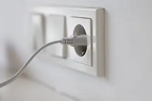 Power Supply Concept Drucke: White power plug in a socket on the wall