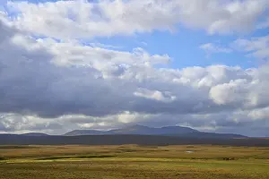 Breite Ebene mit Bergblick und dramatischem Himmel mit dichten Wolken.