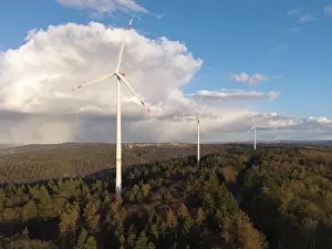 Wind Turbines In Forest Drucke: Wind turbines perch over a thick forest with dramatic clouds in the sky