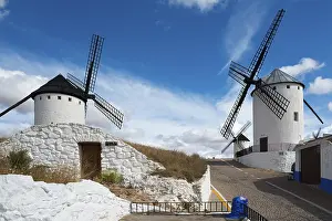 Windmills In Spain Drucke: Two windmills on a hill under a blue sky next to a path