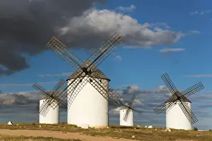 Cloudy Sky Landscapes Europe Drucke: Windmills in a vast landscape under a sky with dramatic clouds and sunlight
