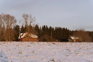 Drucke von Winterwald und Holzhäuser am Abend in einem schneebedeckten Feld, Kernavė, Litauen Litauen Drucke: Winterwald und Holzhäuser am Abend auf einem schneebedeckten Feld.