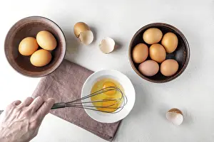 Kitchen Utensil Images Drucke: A woman's hand is beating eggs with a whisk on the kitchen table