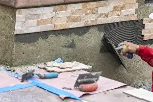 Wall Tile Installation Drucke: Worker installing wall tile cement with trowel and tile at construction site