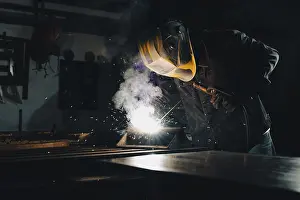Workplace Safety Equipment Drucke: Worker welding an iron plate on the workbench in the workshop