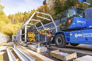 Railway Tunnel Construction Drucke: Workers use cranes to build a structure along a rail line in the forest