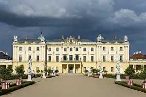 Eastern European Castles Drucke: Yellow baroque castle with statues in the foreground and dramatic clouds