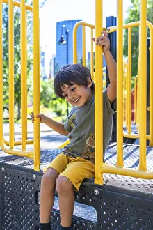 Joyful Facial Expression Drucke: Young boy with a joyful expression sits on a playground structure