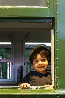 Young Boy Smiling Drucke: A young boy is smiling at the camera from a train window