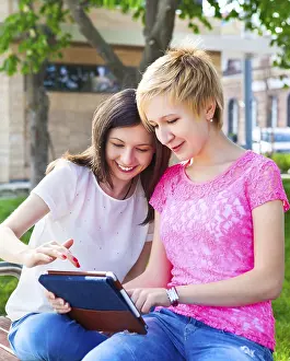 Educational Institution Settings Drucke: Young college students using tablet computer while doing homework in the park