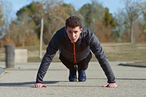 Young Man Fitness Drucke: A young man performs push ups on a concrete path in a park