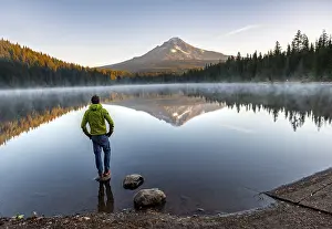 Morning Light On Water Body Drucke: Young man standing on stone, reflection of Mt