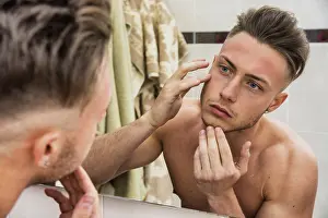 Young Man In Mirror Drucke: Young man touching his face while looking in mirror