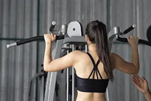 Female Athlete Performance Drucke: A young woman performs pull-ups with the help of her trainer